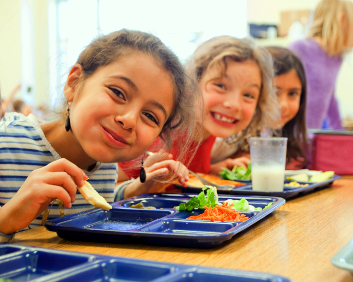 Kids smiling while eating vegetables at their school.
